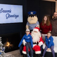 Two siblings with matching blue GVSU zipups with Santa, Louie, and parents